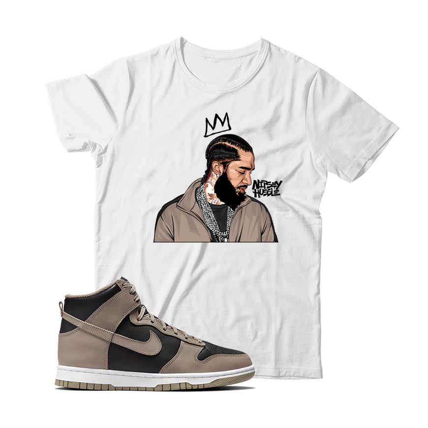 A white T-shirt with an illustration of a male figure wearing a crown and the text 'NIPSEY Hussle', accompanied by a pair of Nike Dunk High Moon Fossil sneakers.