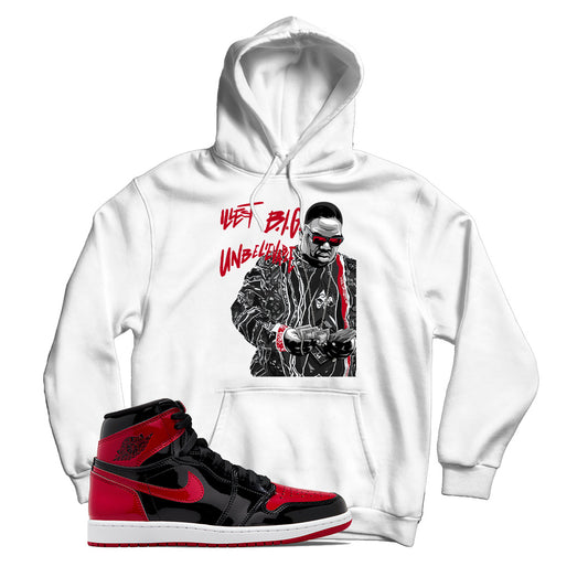 White hoodie with a graphic print of a person wearing sunglasses and a hat, paired with a sneaker matching the Jordan 1 Patent Bred shoe.